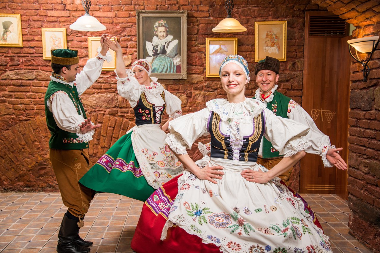 Two women and two men performing a traditional dance in colorful costumes with floral patterns