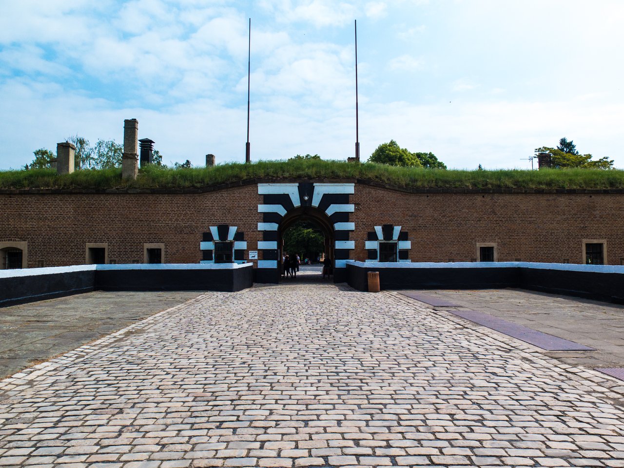 The path leading to the camp's entrance, marked by a black-and-white brick arch, under a blue sky.