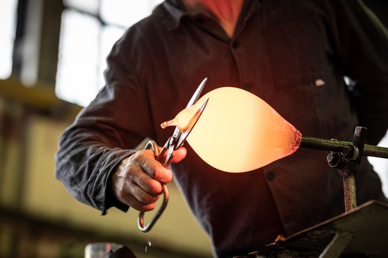 A craftsman using a large chisel to work with hot, orange-colored glass